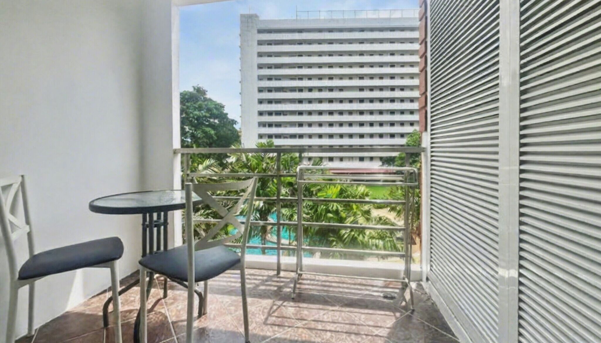 Un balcon doté d’une rambarde en métal, de deux chaises et d’une petite table. On aperçoit un immeuble avec de nombreuses fenêtres à l’arrière-plan.