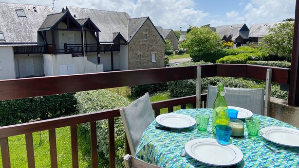 A balcony with a table set for dining, overlooking a row of houses with stone walls and pitched roofs.