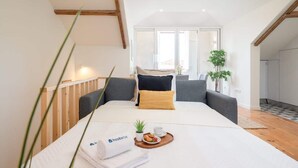 Une chambre d'hôtel moderne avec un grand lit, une table de chevet sur laquelle se trouve un plateau de petit-déjeuner, une fenêtre donnant sur un beau paysage et une plante.