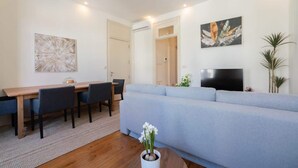 A modern living room with a light blue sofa, a wooden dining table with chairs, a flat-screen TV, and a potted plant. - Modern Comfy Flat by HostWise (Porto)