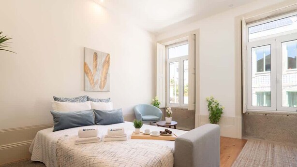 A bedroom with a bed, a chair, a small table, and a window. - Modern Comfy Flat by HostWise (Porto)