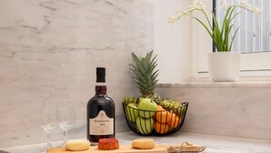 A kitchen with a marble countertop, a bottle of Graham's Tawny Port, a fruit bowl, and a potted plant by a window. - Modern Comfy Flat by HostWise (Porto)