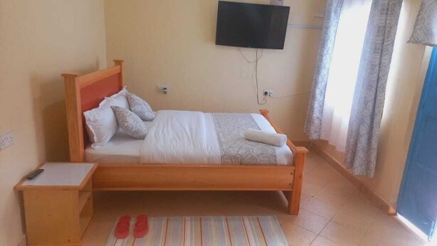 Una cama individual con estructura de madera, un televisor de pantalla plana montado en la pared y un tapete a rayas en el suelo.