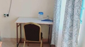 Una habitación pequeña con una mesa, una silla, un televisor en la pared y una cortina.
