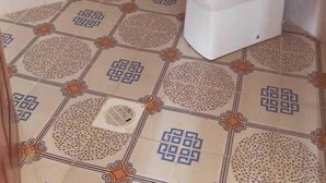 Un baño con inodoro, pisos de baldosas estampadas y dispensador de papel higiénico.