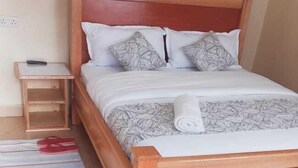 Una cama individual con cabecera de madera, una mesita de noche pequeña y una toalla enrollada sobre la cama.
