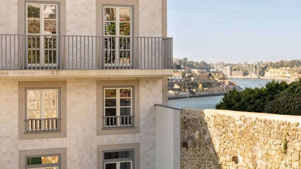 Un edificio de dos pisos con balcones que dan a un río y un puente.