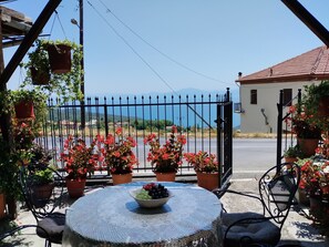 A patio with a round table, potted plants, and a view of the sea and mountains. - Catherine Portaria Guest House (Volos)