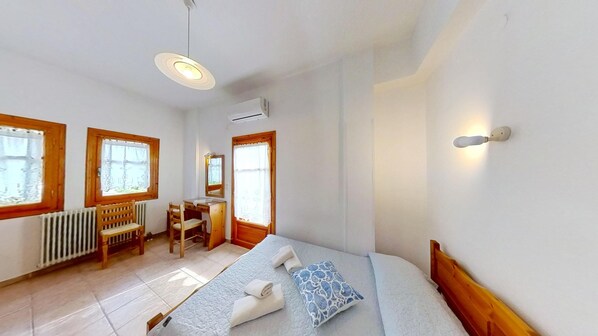 A bedroom with a bed, a desk, a chair, a radiator, and a window. - Catherine Portaria Guest House (Volos)