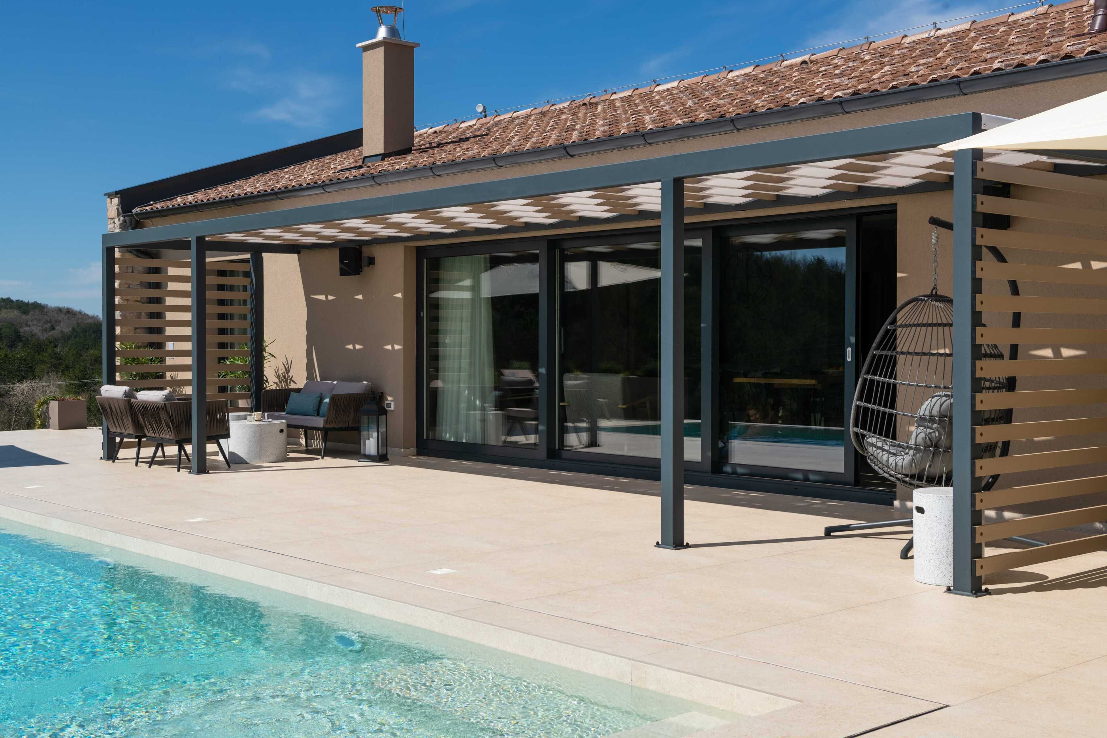 A modern house with a swimming pool, outdoor seating, and a pergola providing shade.