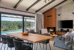 Un salon moderne avec une table à manger en bois, des chaises en osier noir, une cheminée et un grand téléviseur.