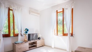 A room with a wooden TV stand, a flat-screen TV, a vase with flowers, and a beige sofa. - Domus Antonini (Massa Lubrense)