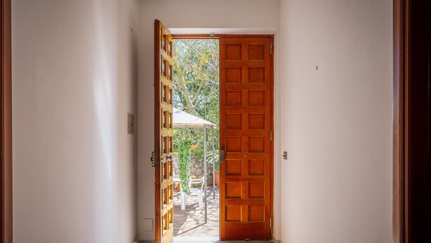 A hallway with a wooden door leading to an outdoor area with a white umbrella and chairs. - Domus Antonini (Massa Lubrense)