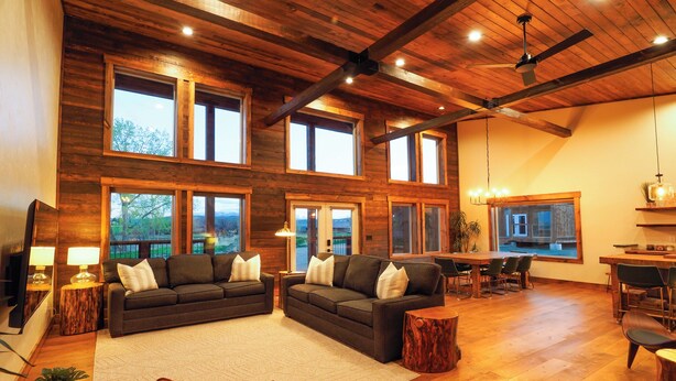 A spacious living area with a high ceiling, large windows, and a wooden interior. - Luxury cabin near Cody: 2 kings, kids bunkroom, fire pit, country charm with easy access. (Cody)