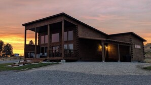 A log cabin with a porch, large windows, and a garage. - Luxury cabin near Cody: 2 kings, kids bunkroom, fire pit, country charm with easy access. (Cody)