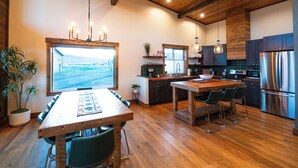 A modern kitchen with wooden flooring, a large island with bar stools, a built-in oven, and a stainless steel refrigerator. - Luxury cabin near Cody: 2 kings, kids bunkroom, fire pit, country charm with easy access. (Cody)
