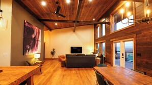 A spacious living area with a wooden ceiling, a large flat-screen TV, a sofa, and a dining table. - Luxury cabin near Cody: 2 kings, kids bunkroom, fire pit, country charm with easy access. (Cody)