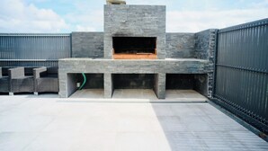 Un patio exterior con una barbacoa de piedra, asientos y una valla de metal.