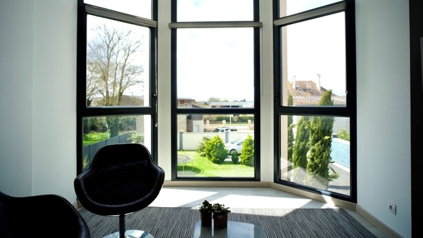 Una habitación con un amplio ventanal que ofrece vistas a un jardín verde, una piscina y un estacionamiento.