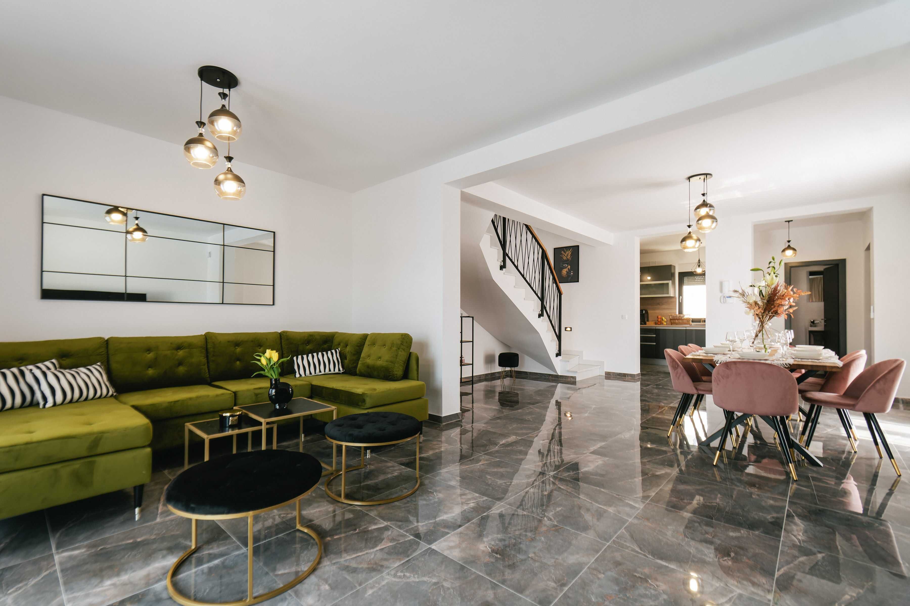 Un salon moderne avec un canapé vert, une table basse noire et un coin repas avec des chaises roses.