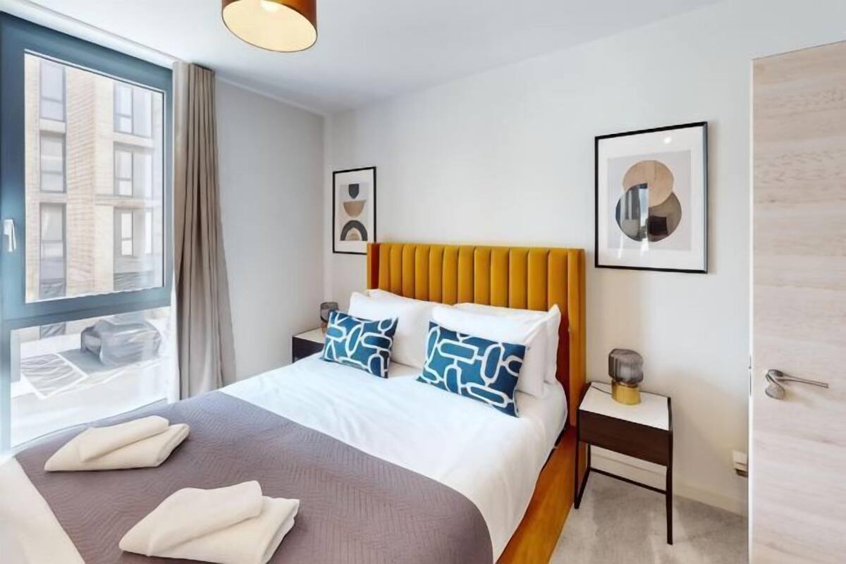 A hotel room with a bed, bedside tables, a window with a view, and framed artwork on the walls.