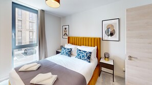 A hotel room with a large bed, a window with a view of the street, a bedside table with a lamp, and a door. - Charles Hope Hove (Hove)