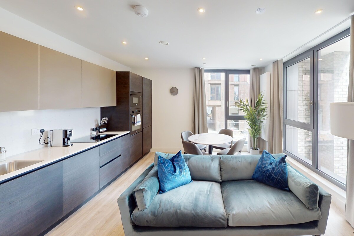 A modern kitchen with built-in appliances, a dining area with a round table, and a sofa with blue cushions.