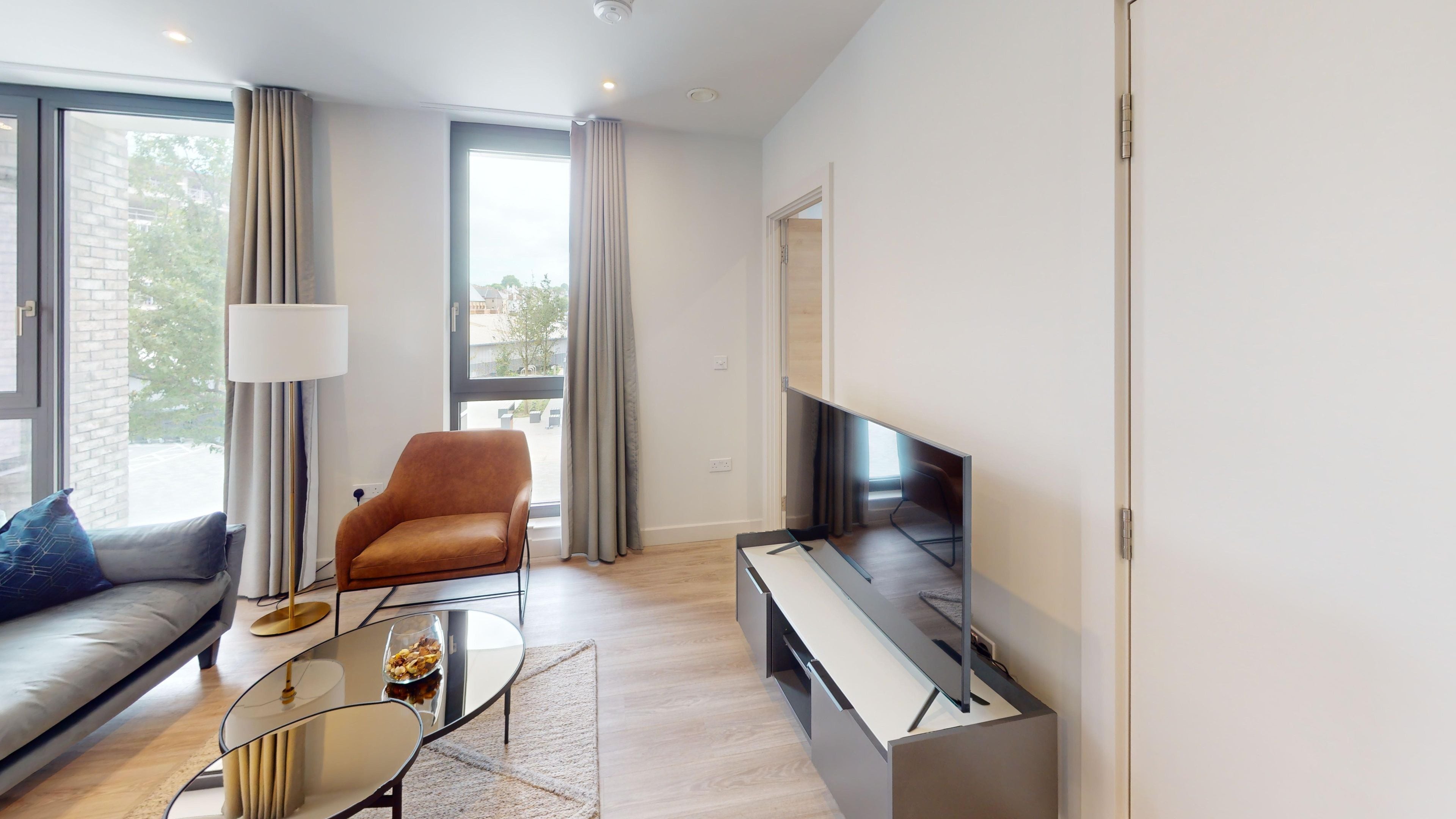 A modern living room with a sofa, armchair, glass coffee table, and a flat-screen TV.