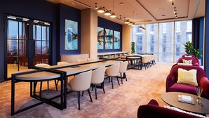 Una sala conferenze moderna con un lungo tavolo, sedie, un divano rosso e ampie finestre con vista sulla città.