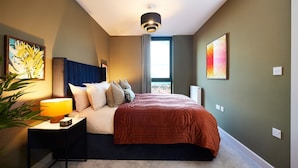 Una camera d'albergo moderna con un letto grande, un comodino con una lampada e opere d'arte alle pareti.