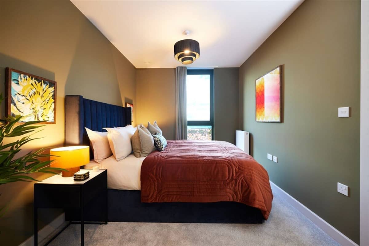 A modern hotel room with a large bed, a bedside table with a lamp, and artwork on the walls.