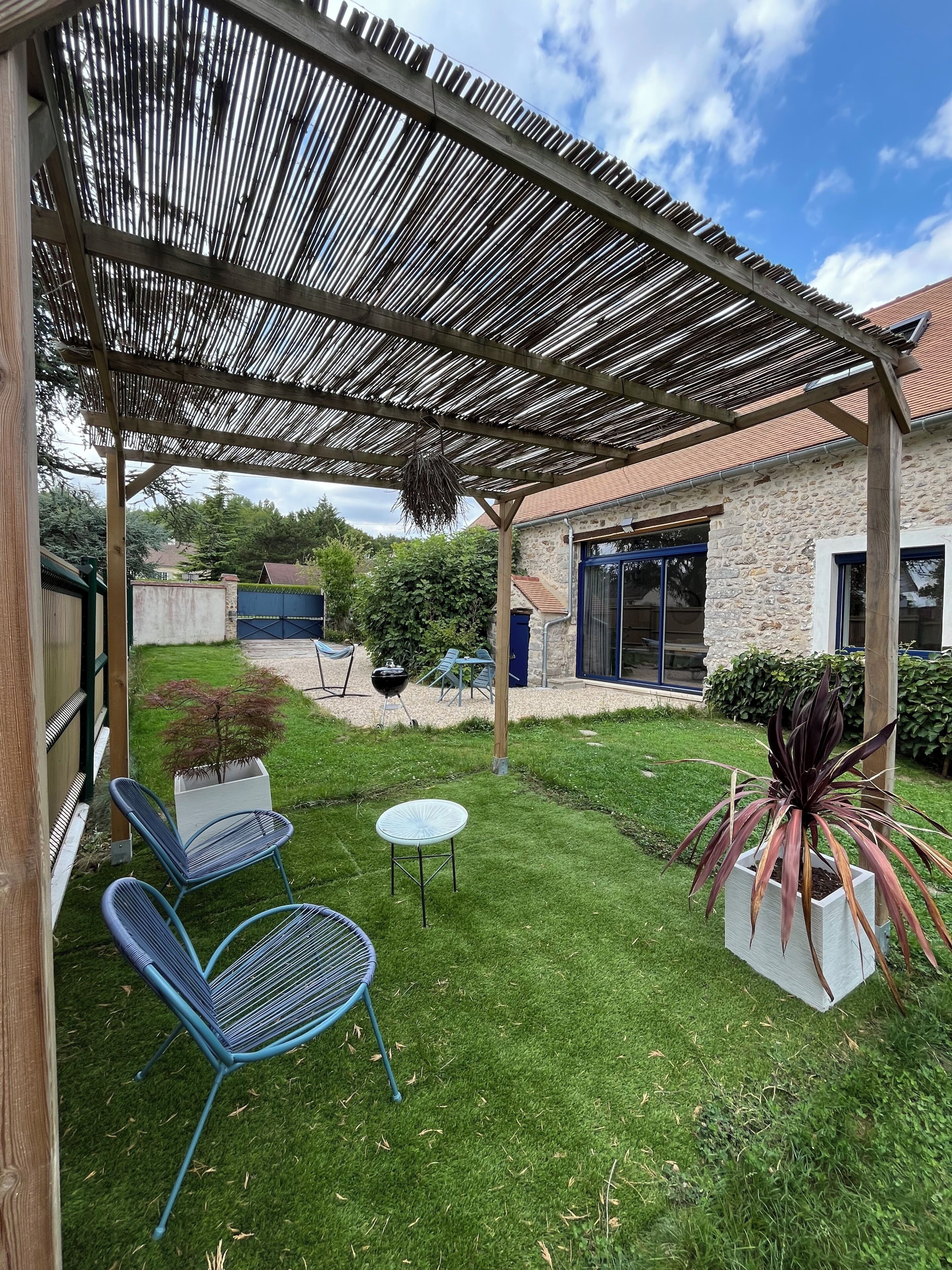 A covered patio with chairs, a small table, and a potted plant.