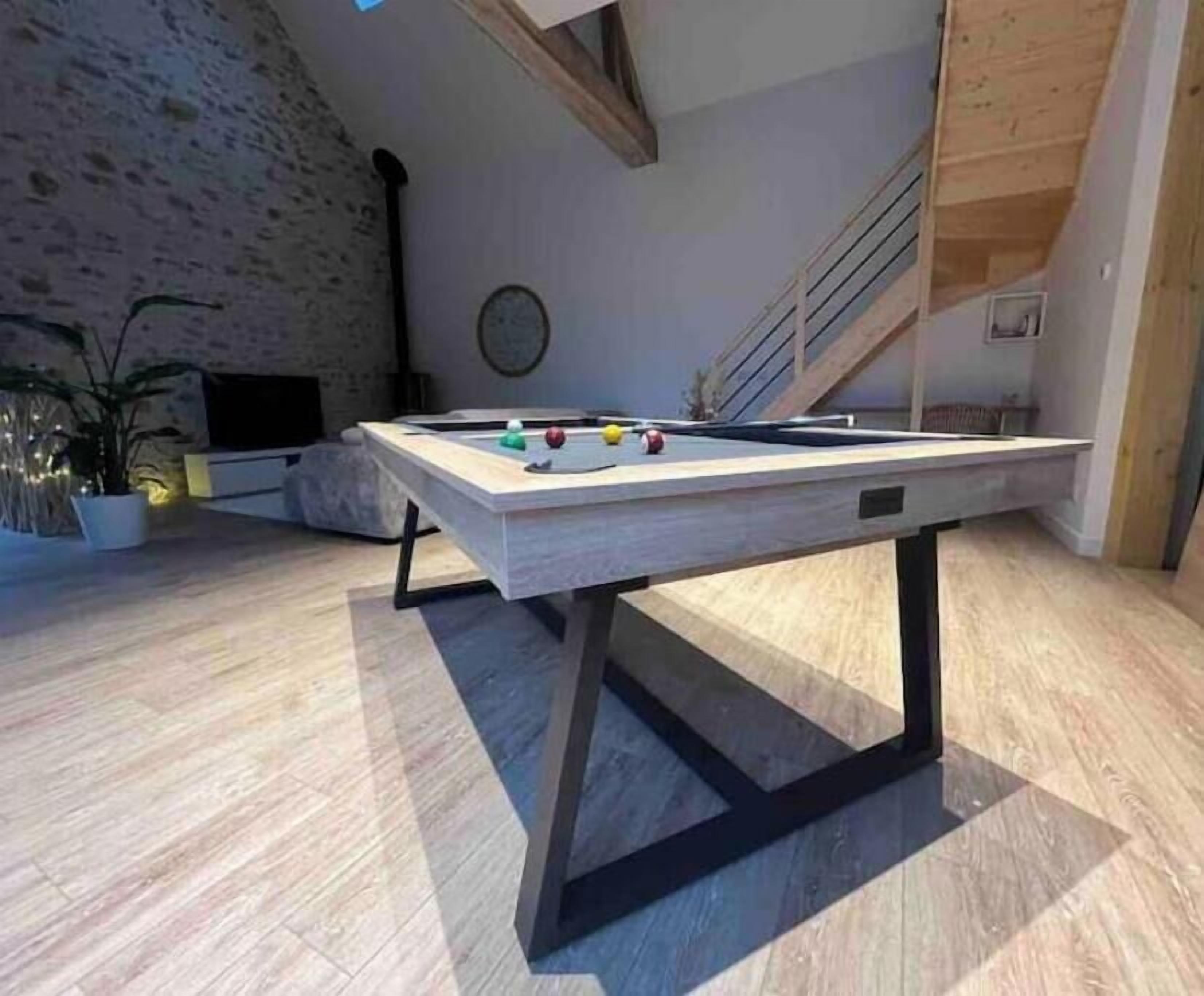 Una mesa de billar en una habitación con techo inclinado, una escalera y una planta en maceta.