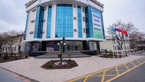 A modern hotel with a large glass facade, a prominent entrance with steps, and a landscaped area with a small tree and a lamp post. - Tantana Hotel (Fergana)