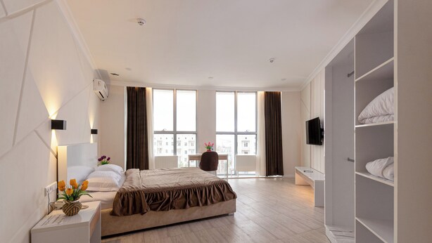 A modern hotel room with a large bed, a bedside table with a lamp, a TV, and a wardrobe. - Tantana Hotel (Fergana)