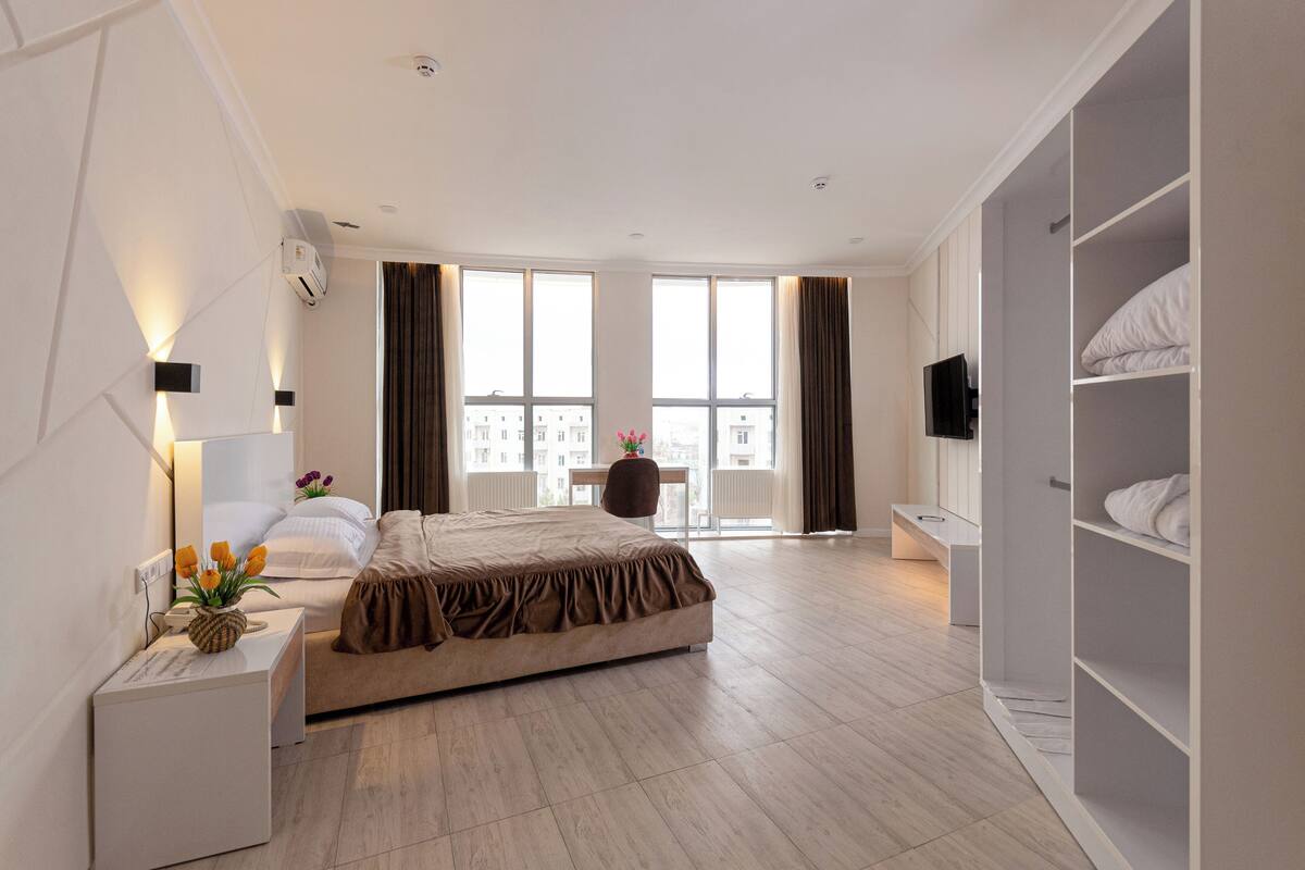 Een moderne hotelkamer met een groot bed, een nachtkastje met een lamp, een televisie en een kledingkast.