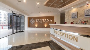 A clean, modern hotel reception area with a polished floor, a reception desk, and a wall-mounted clock displaying the time. - Tantana Hotel (Fergana)