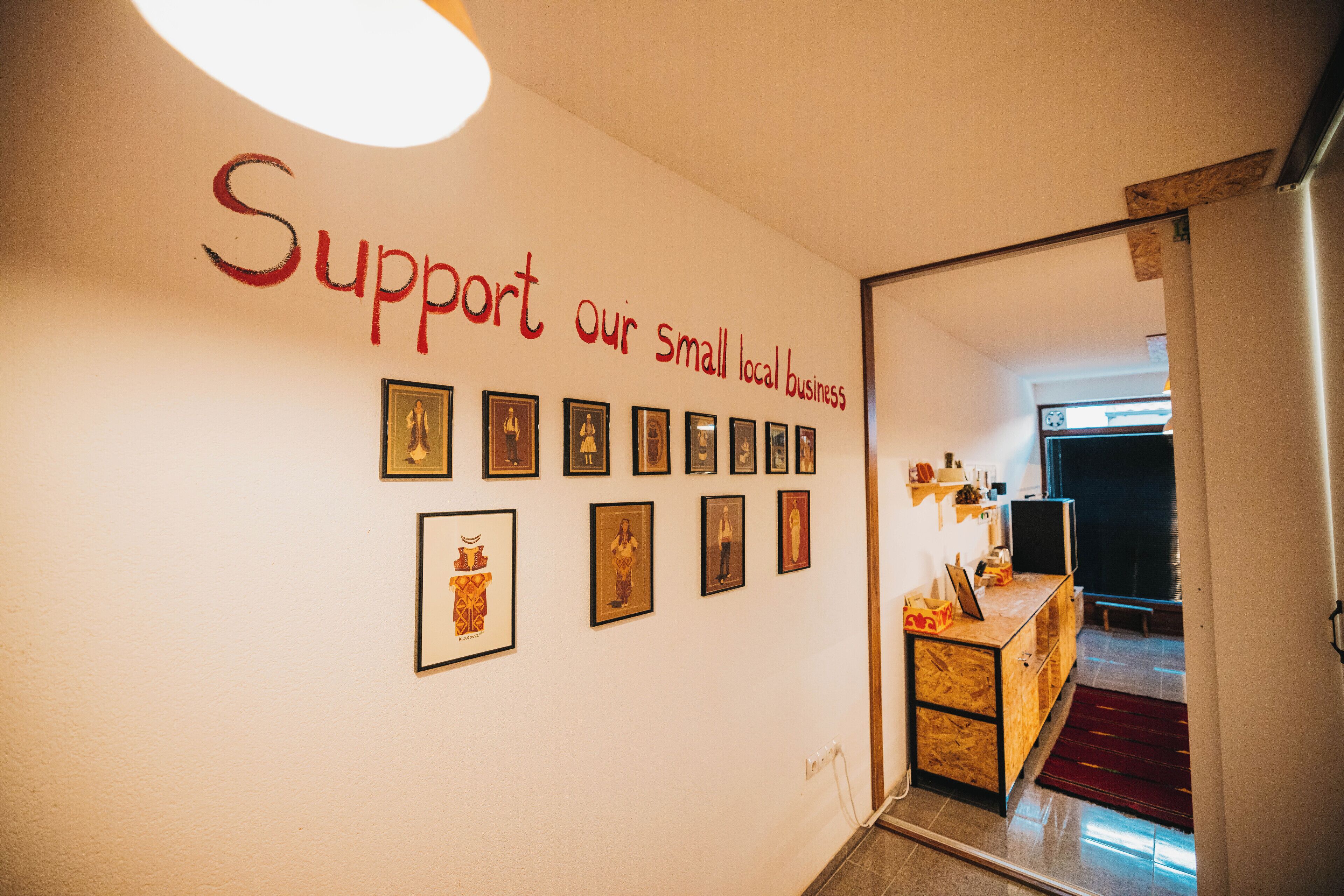 A hallway with a wall displaying a message to support small local businesses, framed pictures, and a wooden counter with a laptop.
