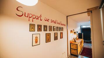 A hallway with a wall displaying a message to support small local businesses, framed pictures, and a wooden counter with a laptop.
