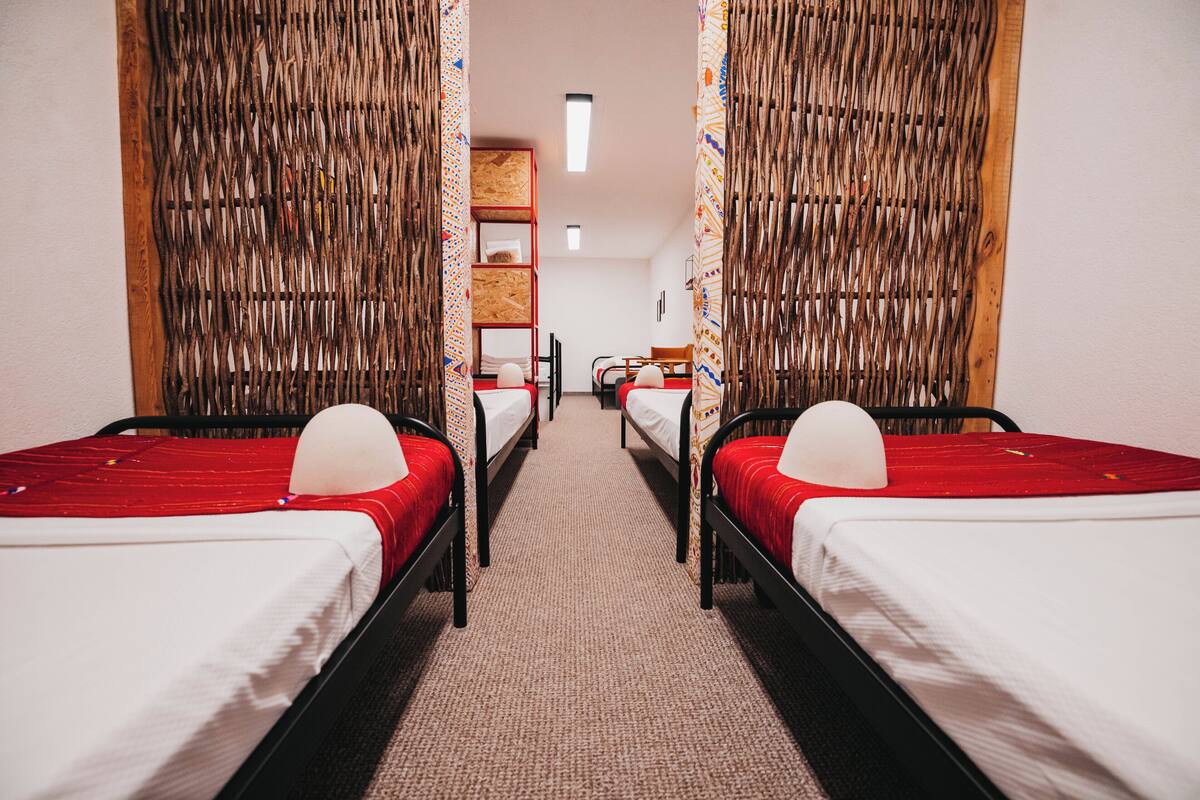 A room with two beds, a wooden shelf, and a chair.