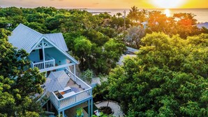 A coastal house with a balcony overlooking the sea, surrounded by lush greenery. - Serenity Oasis~Pool!~Putt-Putt!~Kayaks~Bikes~Spa (Marathon)