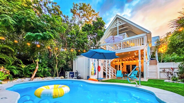 A swimming pool with a floating ring, a covered patio area with outdoor seating, and a two-story building with a staircase leading to the upper level. - Serenity Oasis~Pool!~Putt-Putt!~Kayaks~Bikes~Spa (Marathon)