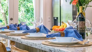 A dining table set with plates, glasses, and a bottle of wine, with a fruit bowl and a vase of flowers in the background. - Serenity Oasis~Pool!~Putt-Putt!~Kayaks~Bikes~Spa (Marathon)