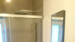 Un baño moderno con un lavabo blanco, un espejo grande y una cabina de ducha de vidrio.
