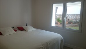 Un dormitorio con una cama, dos almohadas, una ventana y un muro de piedra en el exterior.