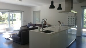 Una cocina moderna con una isla central, un área de comedor con sofá y un amplio ventanal corredera que da a un espacio exterior.