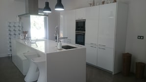 Una cocina moderna con armarios blancos, una isla central con pileta y electrodomésticos de acero inoxidable.