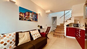 Un salon avec un canapé, une table à manger et un tableau représentant une scène de rue.