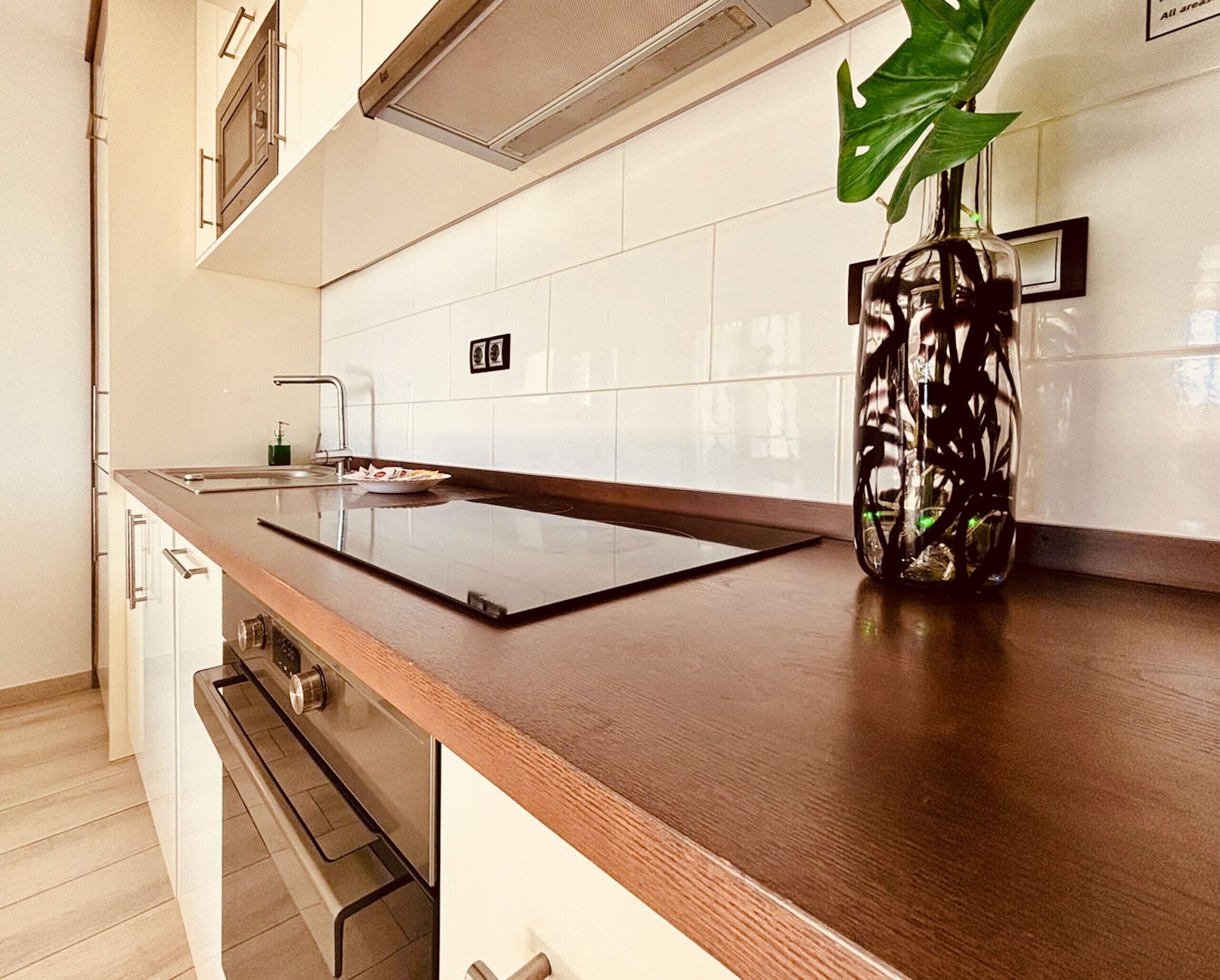 A modern kitchen with a wooden countertop, stainless steel appliances, and a potted plant.