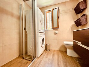 Ein Badezimmer mit Duschkabine, Waschmaschine, Toilette und Holzwaschtisch.